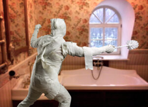 man dress like a mummy holding a toilet brush as if it were a weapon